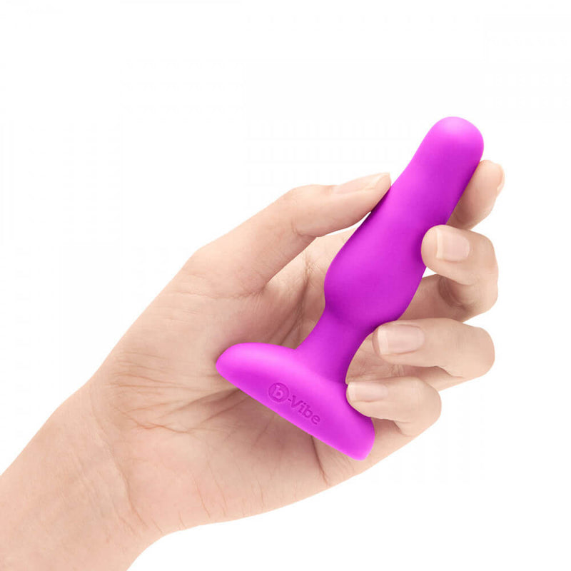 A hand holds the b-Vibe Remote Novice Plug. The plug looks slender and short within the hand. It's slightly thicker than one finger, and it isn't as long as the person's outstretched hand. | Kinkly Shop