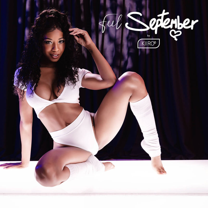 September Reign is kneeling on a lit stage with her legs spread. She's wearing a thin crop top, a white thong, and white leg warmers. | Kinkly Shop