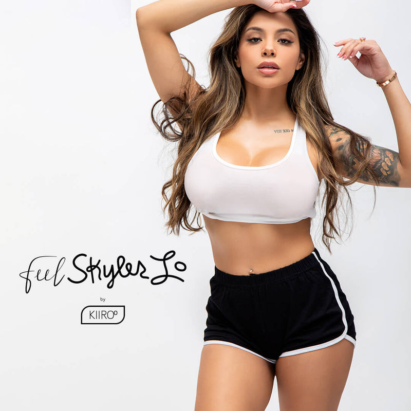 Skyler Lo looks seductively at the camera while wearing a white sports bra and short, black athletic shorts. | Kinkly Shop