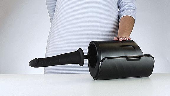 GIF shows the KIIROO KEON Dildo Adapter and Vacuum Lock Dildo partnered together in the KEON. The KEON is turned on, and the dildo is thrusting on top of a table. | Kinkly Shop