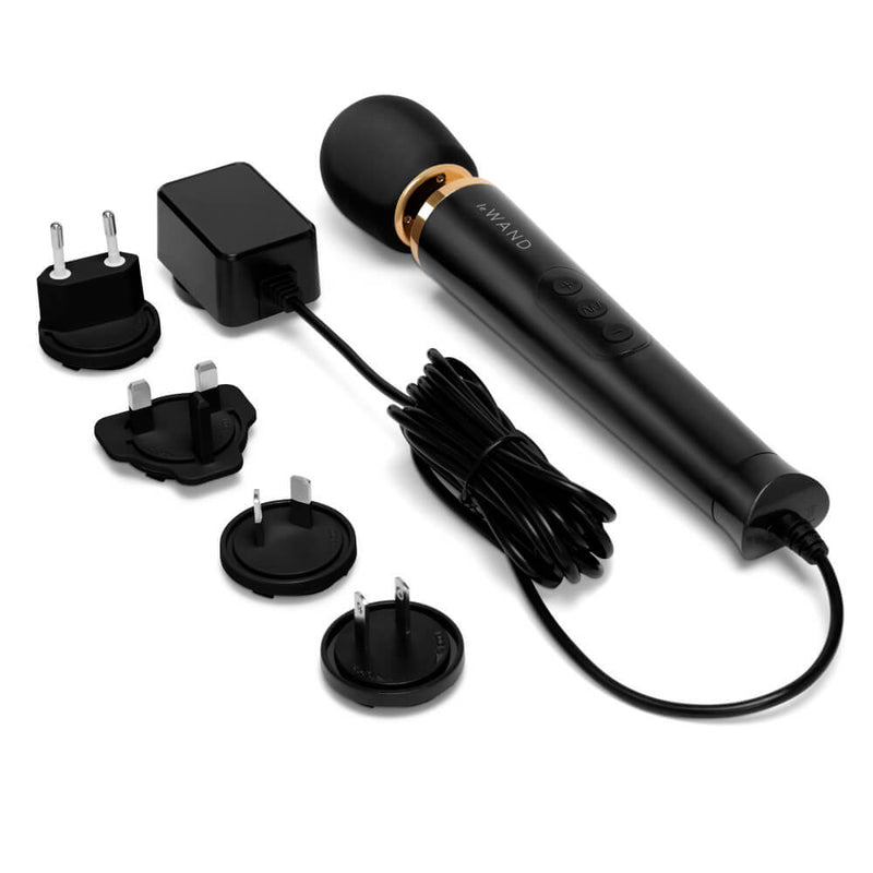 The Le Wand Petite Plug-In Massager in black up against a white background. The power cord is plugged into the wand massager, and the 4 international plates are also laying out next to the wand. | Kinkly Shop