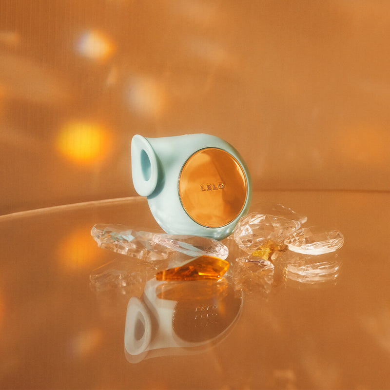 The LELO Sila in Aqua in a copper background, surrounded by gems. The vibrator looks hazy. | Kinkly Shop