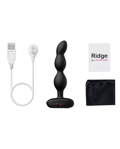 The Lovense Ridge laid out on a white surface next to everything it comes with. There's the Lovense Ridge itself, the charging cable, the drawstring bag, and the instruction manual. | Kinkly Shop