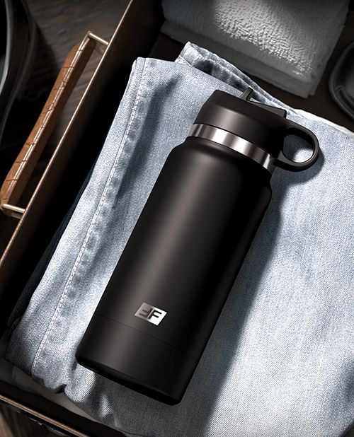 The PDX Plus Fap Flask in Black laying on top of a pair of jeans in someone's luggage. It looks just like a water bottle canteen with no discernible features that would give it away otherwise. | Kinkly Shop