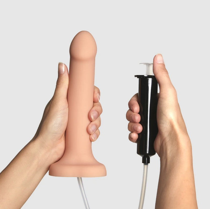 A person's two hands hold the Strap-On-Me Silicone Cum Dildo. One hand holds the dildo in it. The other hand is holding the syringe. The dildo is longer than the person's hand, and the syringe is thick enough that the person's fingers do not close entirely around it. The shape of the syringe means the person's thumb naturally wants to rest on top of the depressor. | Kinkly Shop