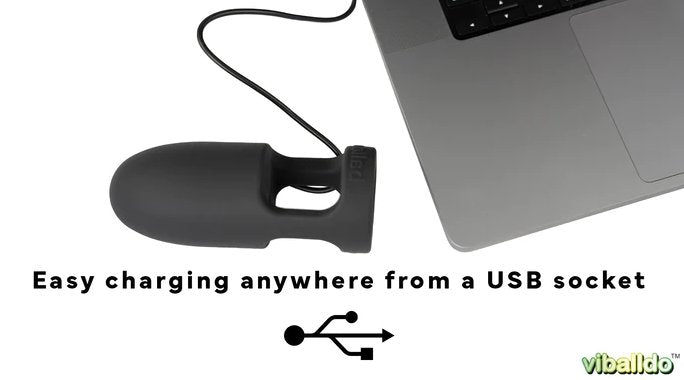The ViBalldo is laying next to the corner of a laptop with a charging cable protruding from it. It looks like the toy is charging from the laptop. Text on the image reads "Easy charging anywhere from a USB socket" | Kinkly Shop