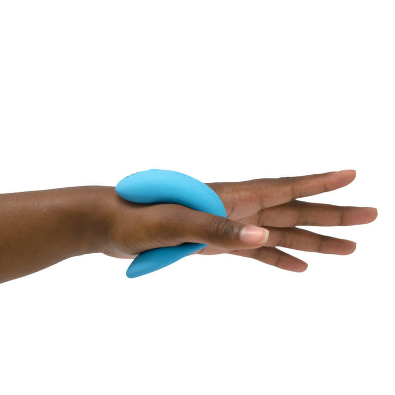 The We-Vibe Chorus shown cinched around a person's palm. One end of the vibrator rests on the top half of their palm while the other end rests underneath their palm, showcasing how the vibrator holds itself, hands-free, in that spot with the tension of the toy. | Kinkly Shop