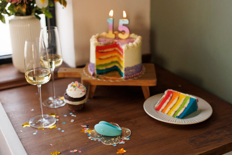 The We-Vibe Sync Lite sitting on a plate on a table. There's a rainbow cake in the background with a slice of the cake on a separate plate. The We-Vibe Sync Lite is slightly longer than the cupcake that's sitting next to it. It isn't as tall as the cupcake. | Kinkly Shop