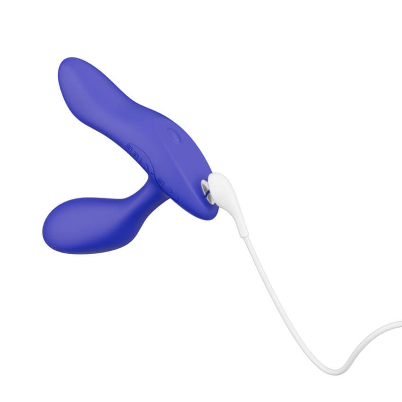 We-Vibe Vector+ up against a white background with the magnetic charging port at the base exposed. A charging cable is shown connecting to the base to showcase how the magnetic charging works. | Kinkly Shop