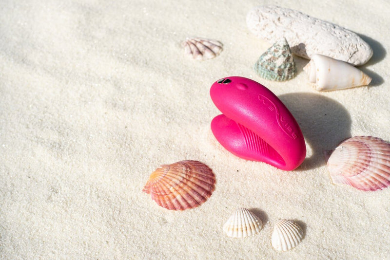 The We-Vibe Chorus sits out on a beach, surrounded by sea shells. | Kinkly Shop
