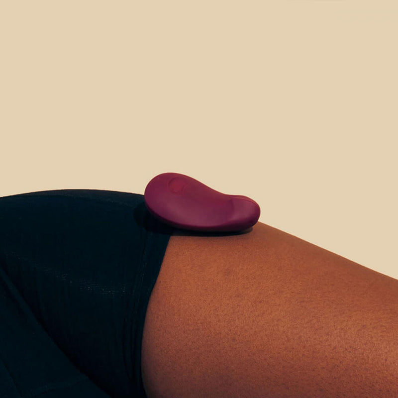The Dame Pom vibrator rests against a person's bare thigh. It looks very small and handheld compared to the person's thigh. | Kinkly Shop