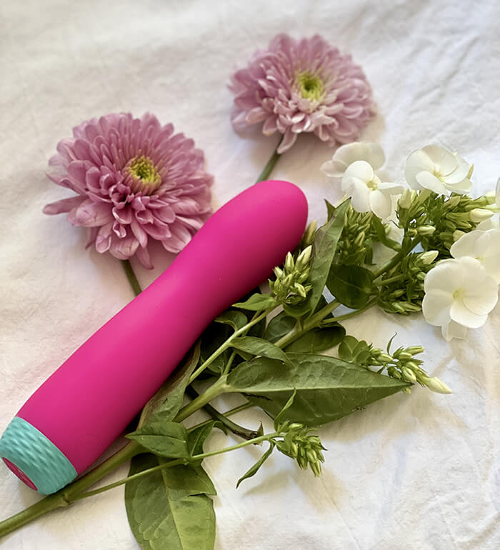The FemmeFunn Rora Rotating Bullet in pink laying on top of a pile of green and pink flowers. | Kinkly Shop
