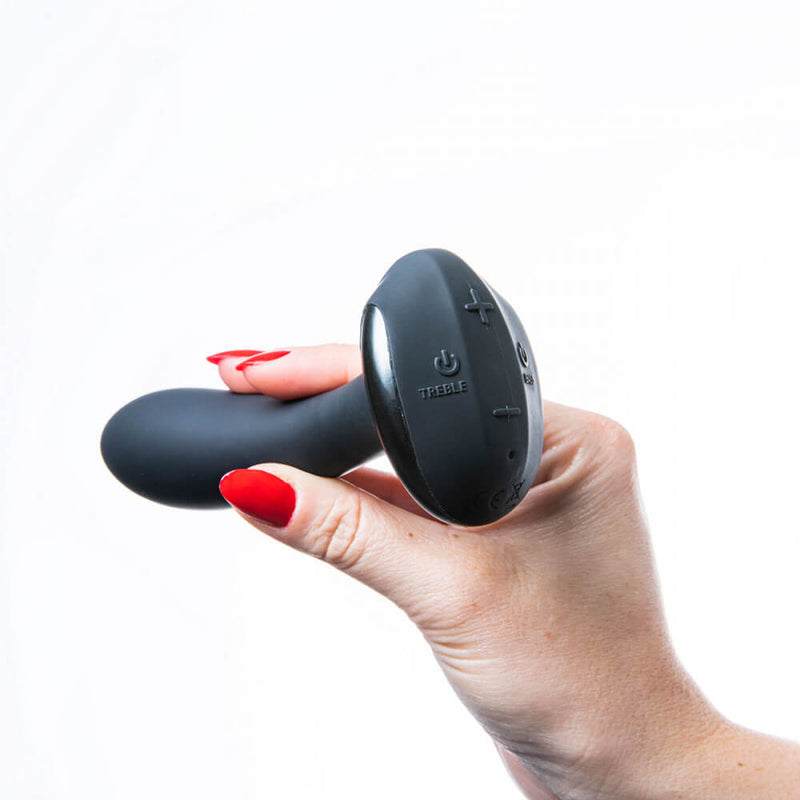 A hand holds the shaft of the Hot Octopuss PleX with Flex while the base points at the camera. This angle clearly shows the control buttons on the base of the anal vibrator. The plus and minus controls are located towards the top and bottom of the oval-shaped base, respectively. The Treble motor power button is on the left-hand side of the oval base while the Bass power button is on the right. | Kinkly Shop