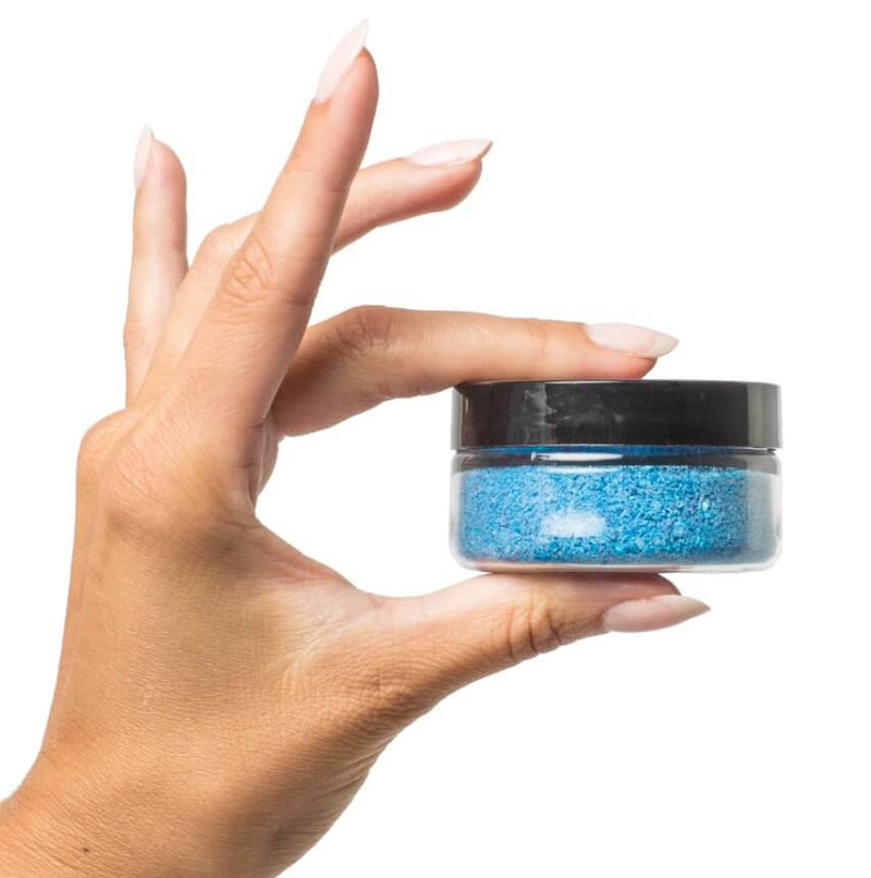 A hand holds the included Treasures of the Sea bath salts container. It looks sized like a travel sized container of body lotion. It is very blue. | Kinkly Shop
