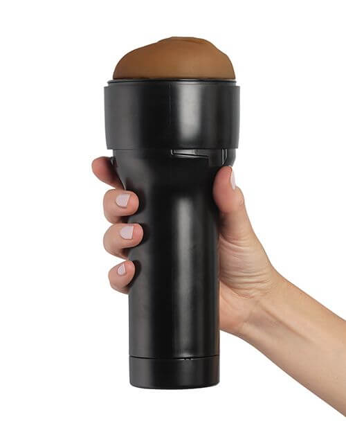 KIIROO RealFeel Generic Vulva in Mid Brown. A hand is wrapped around the base of the stroker. The casing of the stroker offers a lot of space for the hand to rest, and it keeps it away from the internal stroker and the lube. | Kinkly Shop