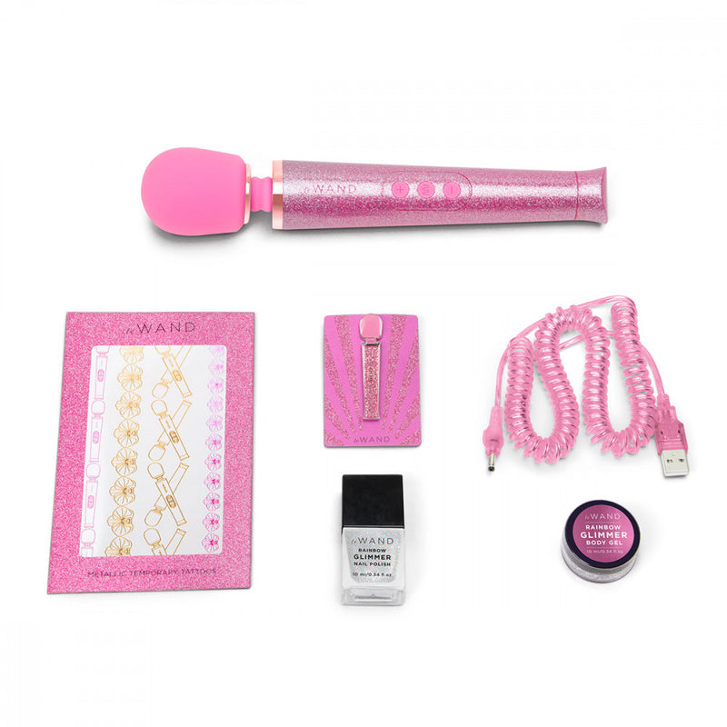 The Pink Le Wand All That Glimmers Wand Massager laid out next to everything that comes with the petite wand massager. That includes the color-coded charging cable, a glittery body gel, a matching enamel pin, a glittery nail polish, and a set of color-matching metallic temporary tattoos. | Kinkly Shop
