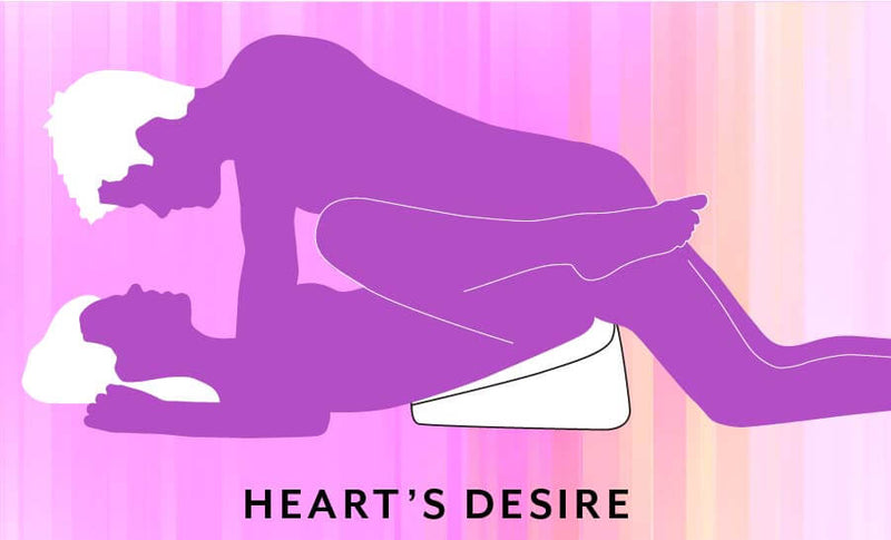 Illustrated sex position called "Heart's Desire". The receiving partner is laying on their back with their hips elevated in the air with the Liberator Heart Wedge. The penetrating partner lays between the receiving partner's thighs to penetrate. This looks like a modified Missionary position; the Liberator Heart Wedge elevating the hips helps provide better g-spot/p-spot stimulation. | Kinkly Shop