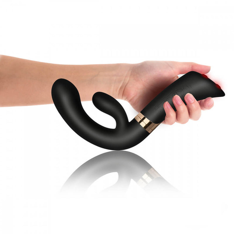 A hand holds the Rocks-Off Enigma Fuzion with the shaft facing towards the hand owner. This angle showcases the drastic curve of the insertable portion of the vibrator to make it easier to grip and use. | Kinkly Shop