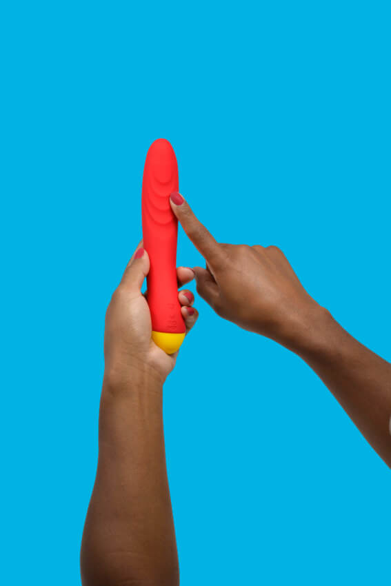Two hands hold the ROMP Hype G-Spot Vibrator in front of a light blue background. One hand holds the base of the vibrator while the other hand's pointer finger points out the ribbing on the curved, g-spot end of the vibrator. The vibrator is clearly much thicker than a single finger, and it's much longer than a person's hand. | Kinkly Shop