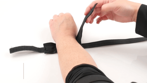 GIF showing a person laying their wrist flat into one of the cuffs. They then velcro the cuff onto their wrist and pull snug to show the durability. The text says "Adjustable cuffs for easy on, easy off play". The GIF then moves to the person handling the Soft Blindfold. | Kinkly Shop
