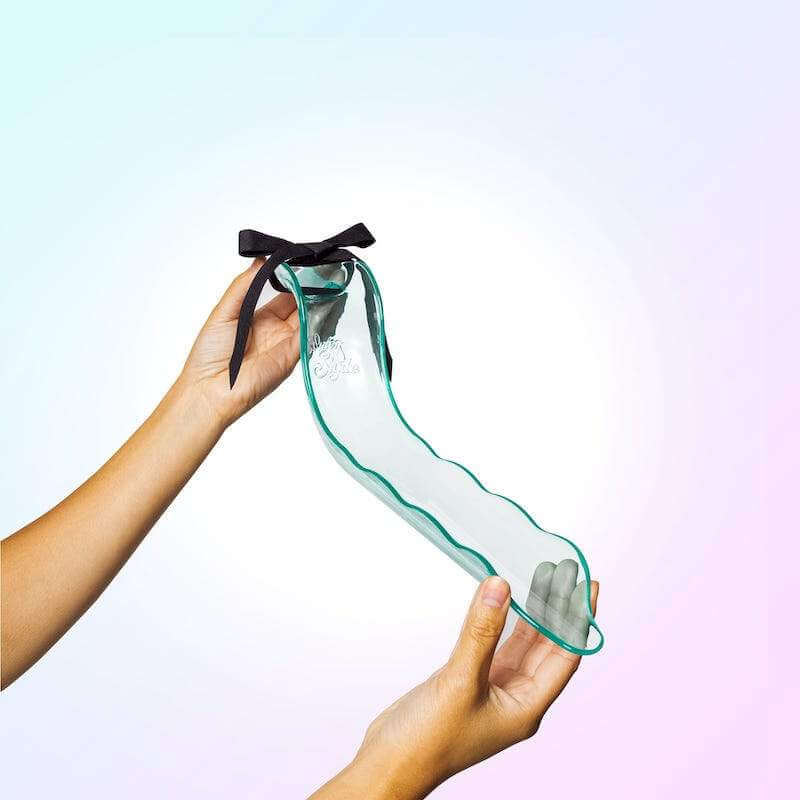 Two hands hold the aqua Waterslyde Bathtub Water Diverter. You can see the ribbon on the top and the downward trajectory of the spout. | Kinkly Shop
