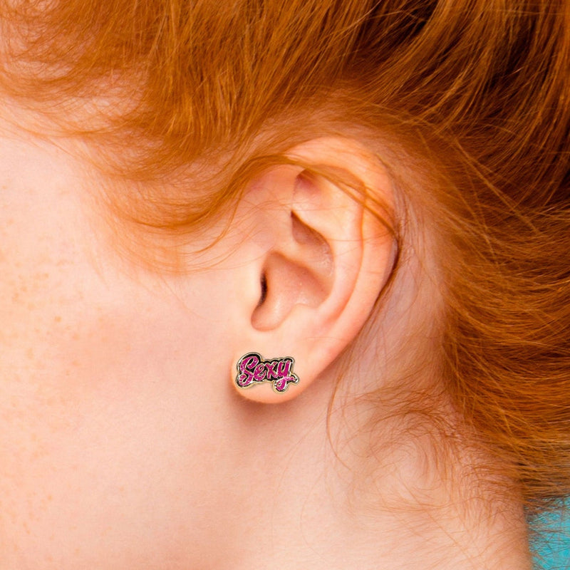 WoodRocket "Sexy" Word Earrings shown in the ear of a red-headed person | Kinkly Shop