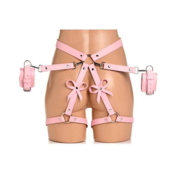A mannequin wears the Strict Bondage Harness with Bows in pink. The optional cuffs are fastened onto the hip harness' O-ring as well. | Kinkly Shop