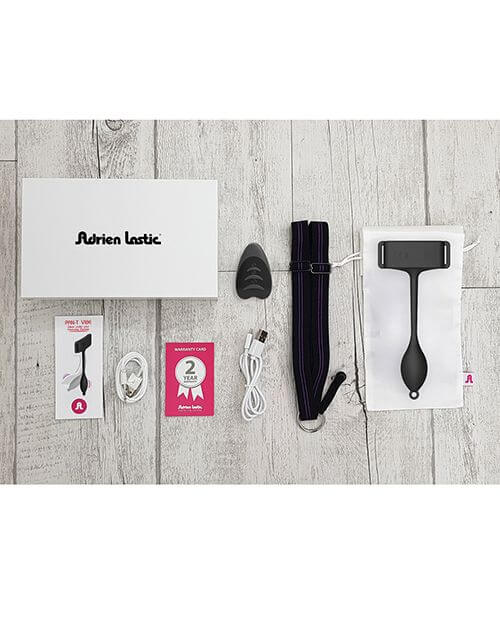 Everything that's included with the Adrien Lastic Pan-T Vibrator shown laid out on top of wooden flooring. It includes the vibrator itself, the harness for it, the remote control, the charging cable, warranty information, and an instruction manual. | Kinkly Shop