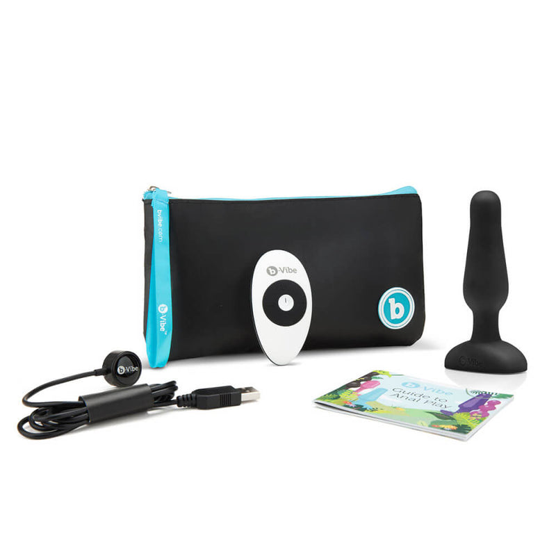 The b-Vibe Remote Novice Plug with everything it comes with. This includes the Novice plug itself, the remote control for it, a Guide to Anal Play, the charging cable, and a zippered, branded pouch to keep all of the items together. | Kinkly Shop