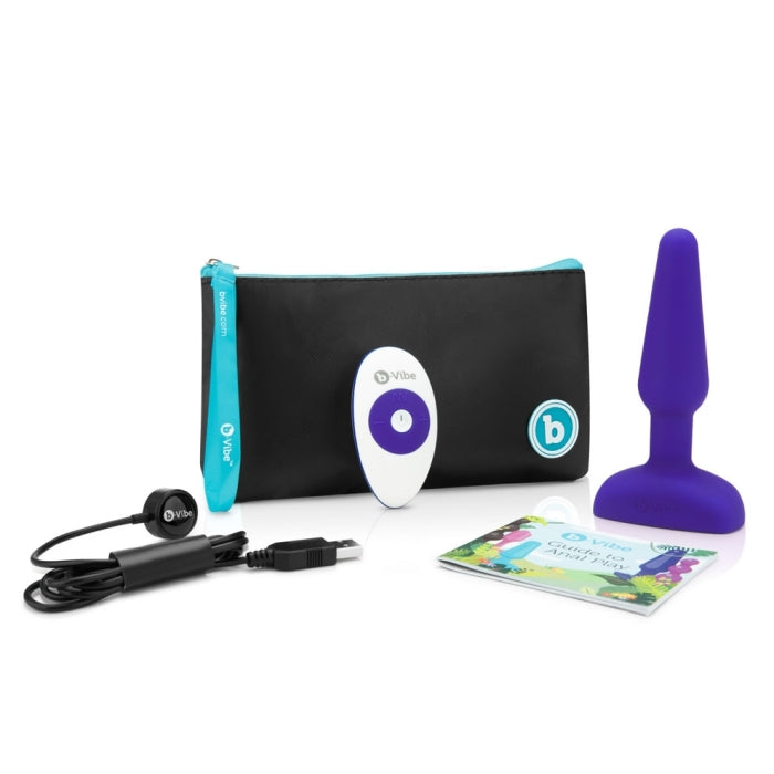 The b-Vibe Remote Trio Plug in purple alongside everything it comes with in front of a white background. There's the plug itself, the remote, the charging cable, the Guide to Anal Play booklet, and the zippered carrying pouch for all of it. | Kinkly Shop