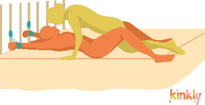 Classic Bed Bondage sex position. The bound partner is lying flat on their back with their hands held above their head at the headboard. Cuffs are fastened around their wrists that are fastened to the headboard. Their partner is kneeling overtop of them.