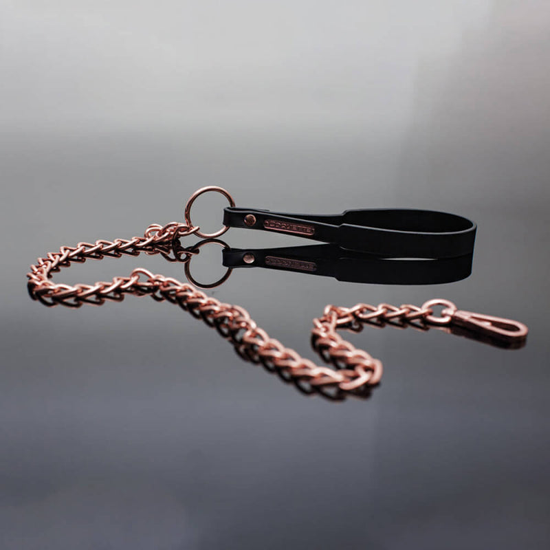 The Coquette Black and Rose Gold Leash up against black gradiant background. The rose gold and black stand out against the black background, looking sultry and shiny against the background. | Kinkly Shop