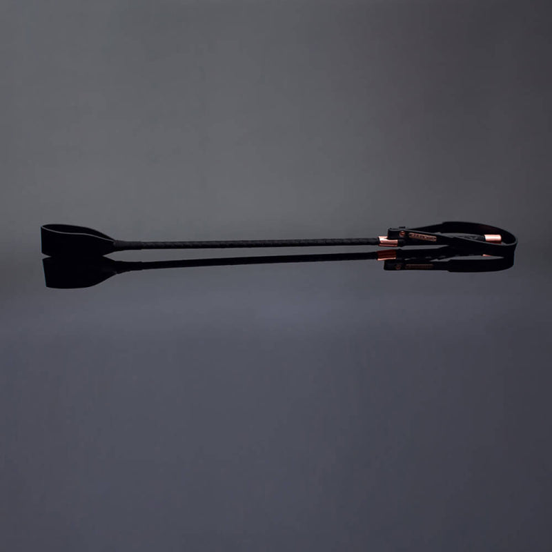 Coquette White and Rose Gold Riding Crop against a black background. It looks dark and sultry with the midnight, shadowy vibes of the entire image. | Kinkly Shop