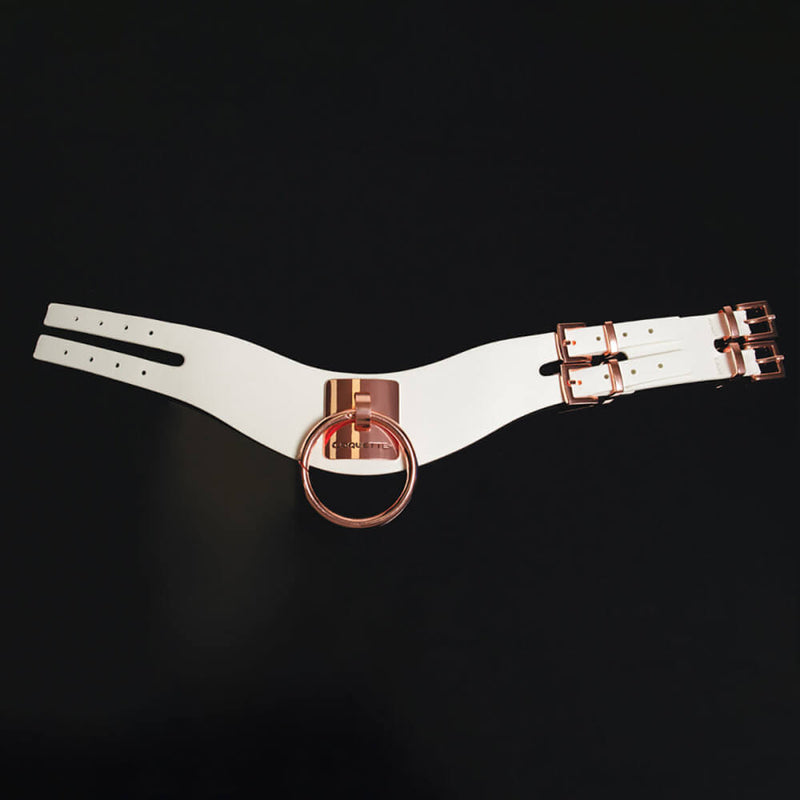 The Coquette Pleasure Collar in white laid flat on top of a black background with a top-down view. The collar has two buckles and two straps that wrap around the back side of the neck. The Rose Gold hardware is found on all metal pieces of the collar for a beautiful contrast with the white. | Kinkly Shop
