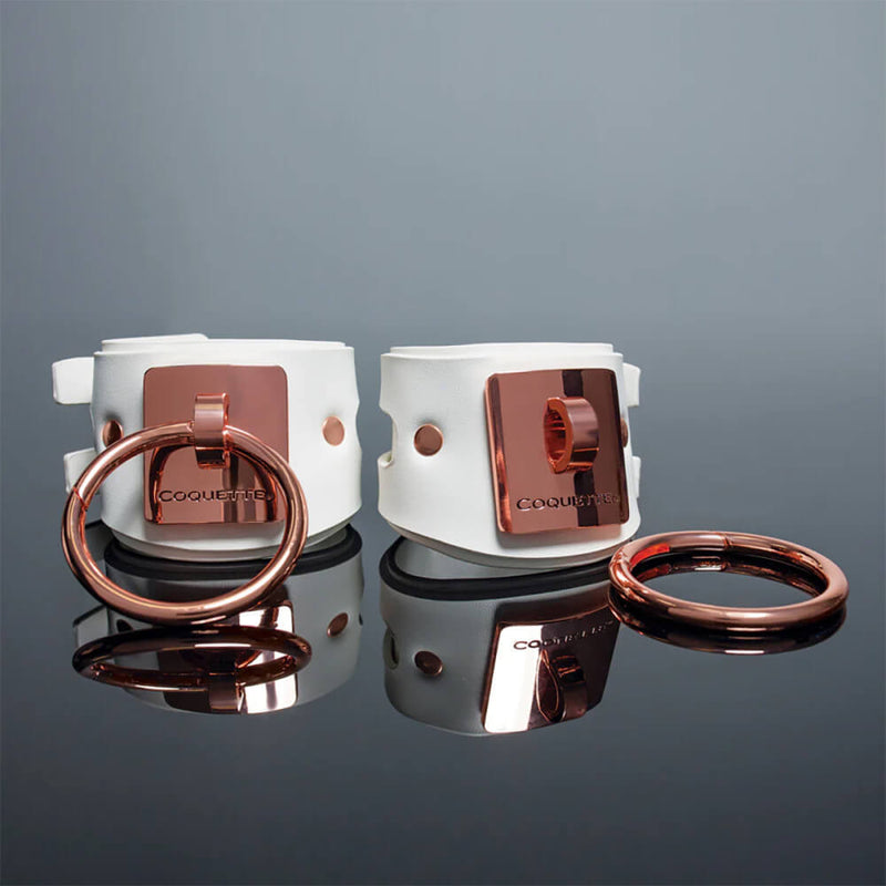 The two Coquette White and Rose Gold Adjustable Cuffs sit next to one another. The large O-ring has been removed from the plates of one of the cuffs to showcase the potential change if you'd like. | Kinkly Shop