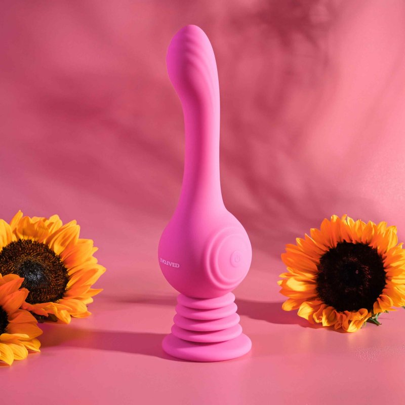 A bright, lifestyle image of the Evolved Gyro Vibe. It is shows in front of a pink background. Against the pink background, shadows of leaves can be seen. In the foreground, there are bright yellow sunflowers for visual interest. It looks like a fun, playful image. | Kinkly Shop