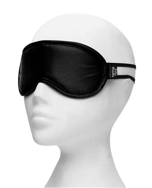 The blindfold included with the Fifty Shades of Grey Come to Bed Kit. It is a satin blindfold that includes two elastic bands that wrap around the back of the head to hold the blindfold in place. It is shown on a mannequin head. | Kinkly Shop