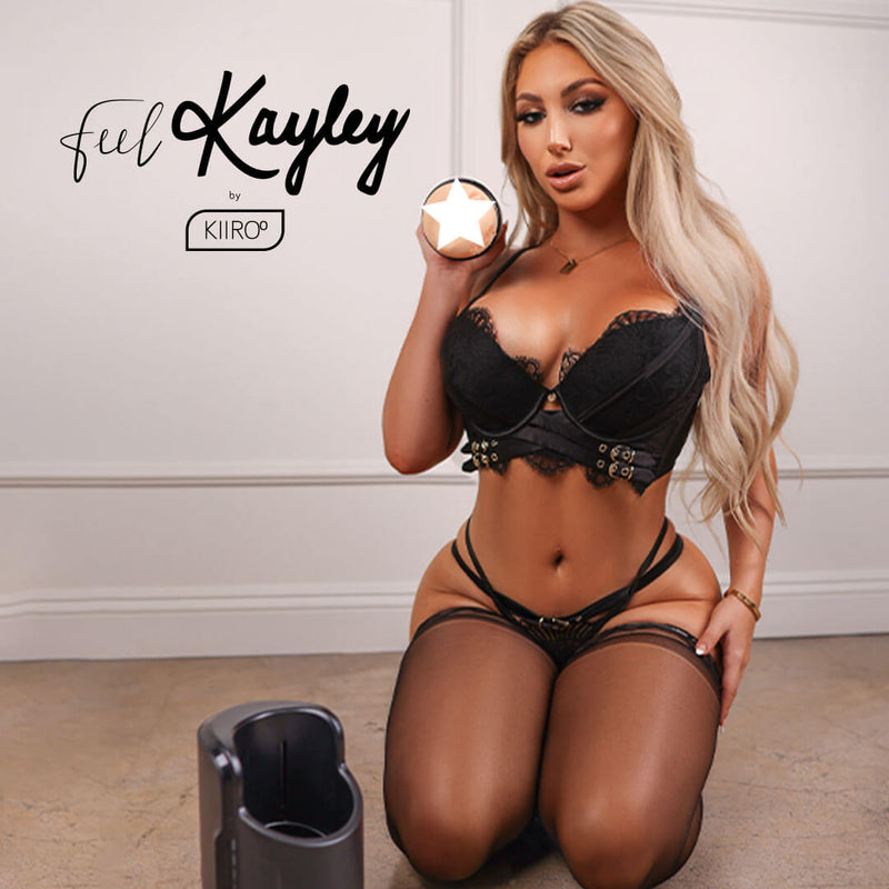 Kayley Gunner in lacy black lingerie, kneeling on the floor. She's holding her KIIROO FeelStars FeelKayley Stroker in her hand, and the KEON is resting on the floor in front of her. | Kinkly Shop