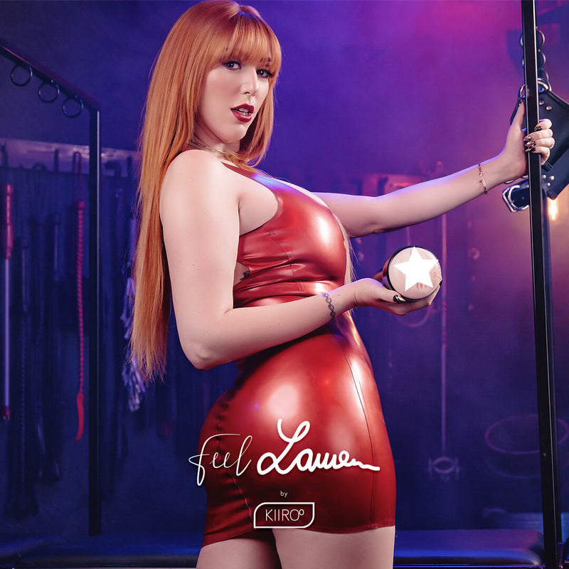 Lauren Phillips standing in a dungeon and gripping onto a bondage frame. She's wearing a skintight red latex dress. One of her hands is holding the KIIROO FeelStars FeelLauren Stroker | Kinkly Shop