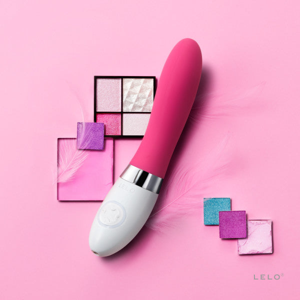 The LELO LIV 2 up against a pink background. Make-up palette colors are scattered around the LELO LIV 2, showcasing accent colors that make the vibrator's pink color stand out more. | Kinkly Shop