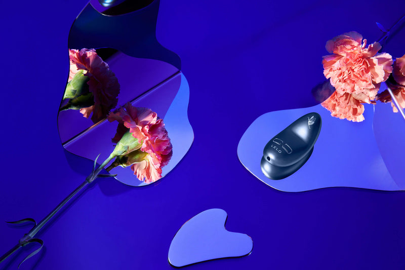 The LELO NEA 3 in Alien Blue in the middle of a blue-focused decorative scene. Lots of mirrors offer depth while a few pink flowers add contrast. | Kinkly Shop