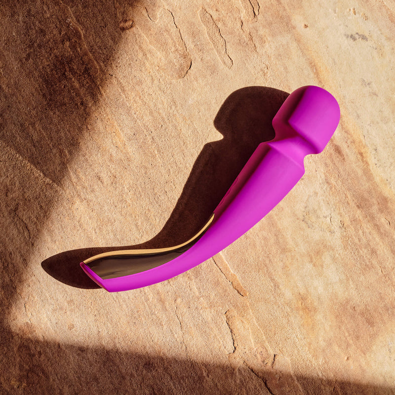 LELO Smart Wand 2 Medium in Deep Rose laying on top of a stone flooring. A hard beam of sun is lighting the massager for a very beautiful visual that showcases the bright deep rose color. | Kinkly Shop