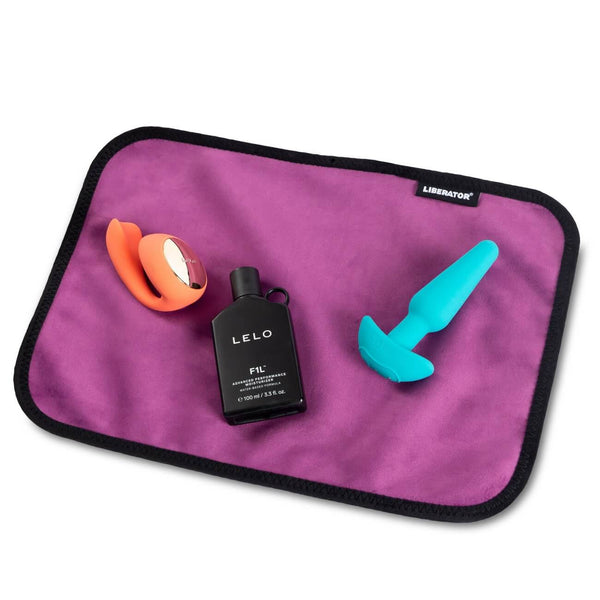 Two sex toys and a bottle of full-sized lube sit out on a purple Liberator Fascinator Toy Pad. There's a ton of extra room to spare around all of the items. | Kinkly Shop