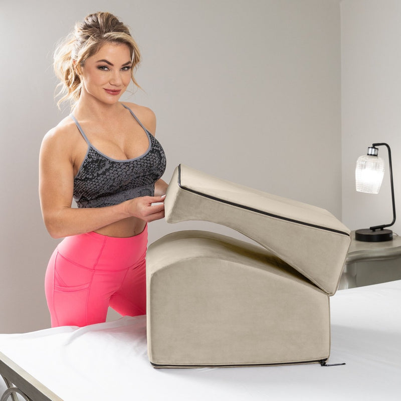 A person in athletic clothing is standing next to a bed. The Liberator Flip Ramp is on the bed, folded up. The person is lightly lifting one end of the Flip Ramp, showcasing how the two sides of the Flip Ramp unfold to reveal the entire, curvy shape of the Liberator Flip Ramp. | Kinkly Shop