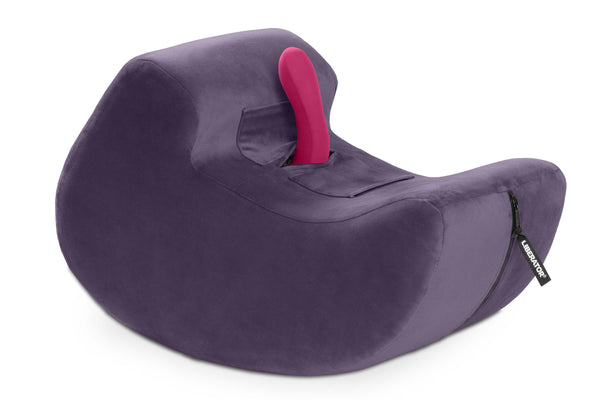 The Liberator Pulse in Purple up against a plain white background. A pink vibrator is protruding from the center of the shape at an angle that would make it easy to ride or grind against. The Pulse has a shape like a sideways comma with a rocking base that allows the shape to rock backwards and forwards with ease. | Kinkly Shop