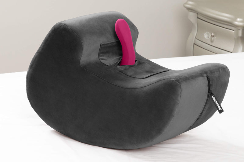 The Liberator Pulse in Black up against a plain white background. A pink vibrator is protruding from the center of the shape at an angle that would make it easy to ride or grind against. The Pulse has a shape like a sideways comma with a rocking base that allows the shape to rock backwards and forwards with ease. | Kinkly Shop