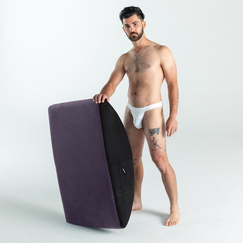 A person stands next to the Liberator Scoop Rocker. They are holding the Scoop Rocker upright, on one of its edges, and the Rocker's height reaches the person's belly button. | Kinkly Shop