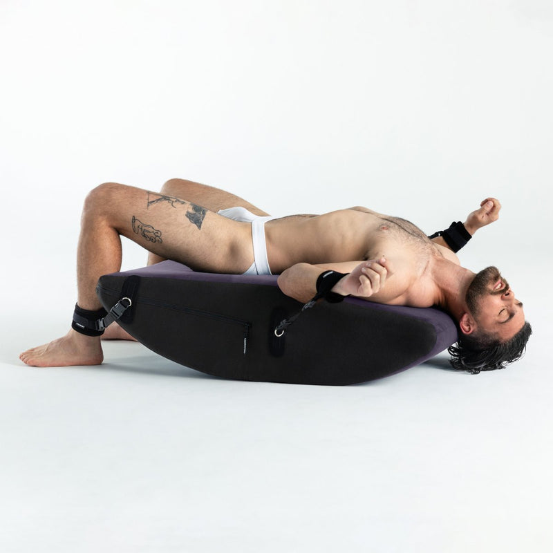 A person in their underwear is laying on their back on top of the Liberator Scoop Rocker. Their wrists and ankles are restrained to the Scoop shape beneath them. The Scoop's length fits the person's body from knees to shoulders with no issue. | Kinkly Shop