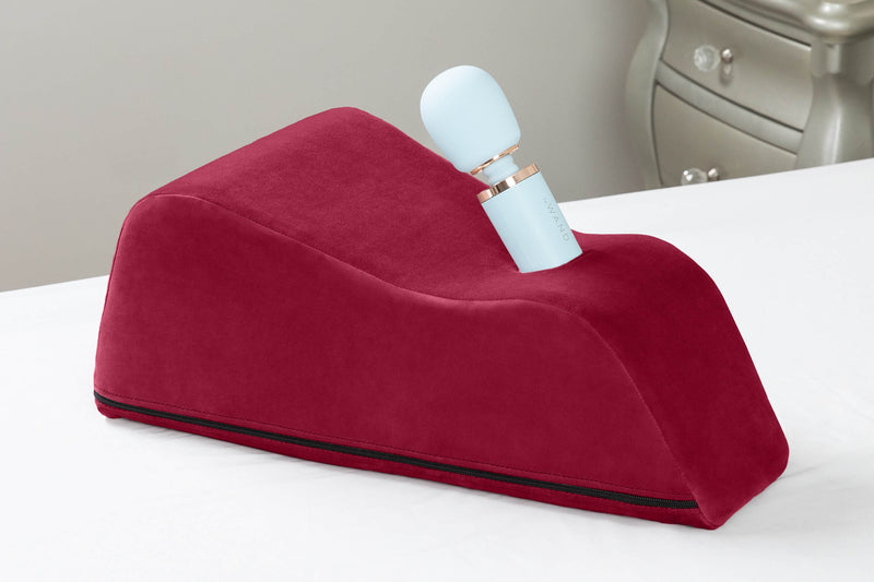 Close-up of the Liberator Wanda in Merlot resting on top of bed with white bedding. | Kinkly Shop
