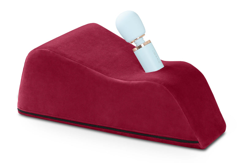 The Liberator Wanda in Merlot up against a plain white background. There's a blue wand massager sitting in the Wanda is protruding upwards at an angle. | Kinkly Shop